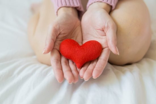 Mujer sosteniendo un corazón rojo, simbolizando cómo la fibra de la manzana ayuda a reducir el riesgo de enfermedades cardiovasculares.