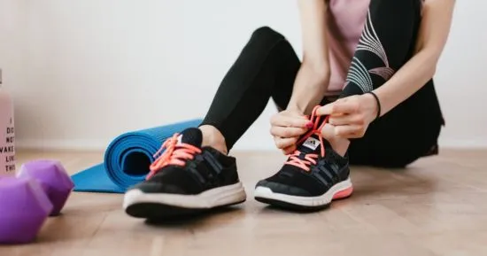 Mujer atándose las zapatillas deportivas antes de hacer ejercicio, un ejemplo de la diferencia entre actividad física personal y un deporte competitivo.