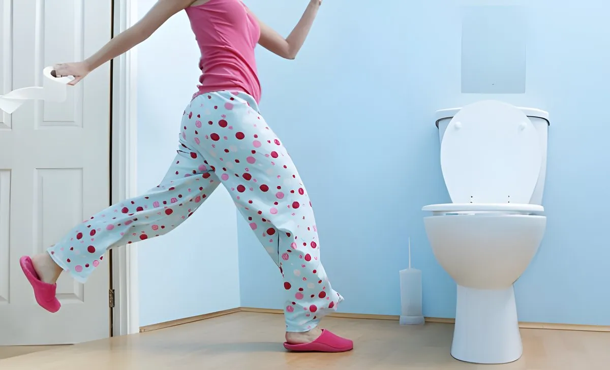 Mujer en pijama corriendo con urgencia al baño, un síntoma claro de una infección de orina o cistitis.