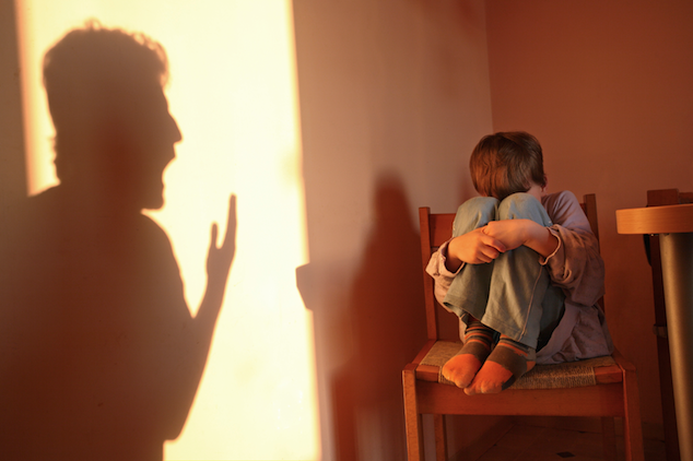 Niño acurrucado en una silla mientras la sombra de un adulto le grita, representando el trauma de la violencia doméstica.