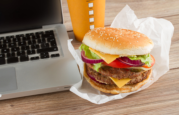 Hamburguesa y gaseosa junto a una laptop, simbolizando la mala alimentación en el trabajo