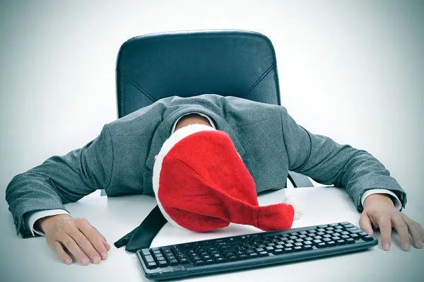 Estrés de fin de año: evita llegar muy agotado Hombre dormido sobre su escritorio con una gorra de Santa Claus, simbolizando estres de fin de año