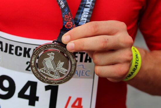 La Recompensa de Correr un Maratón Primer plano de un corredor sosteniendo con orgullo su medalla de finisher de maratón, con el dorsal de la carrera visible.