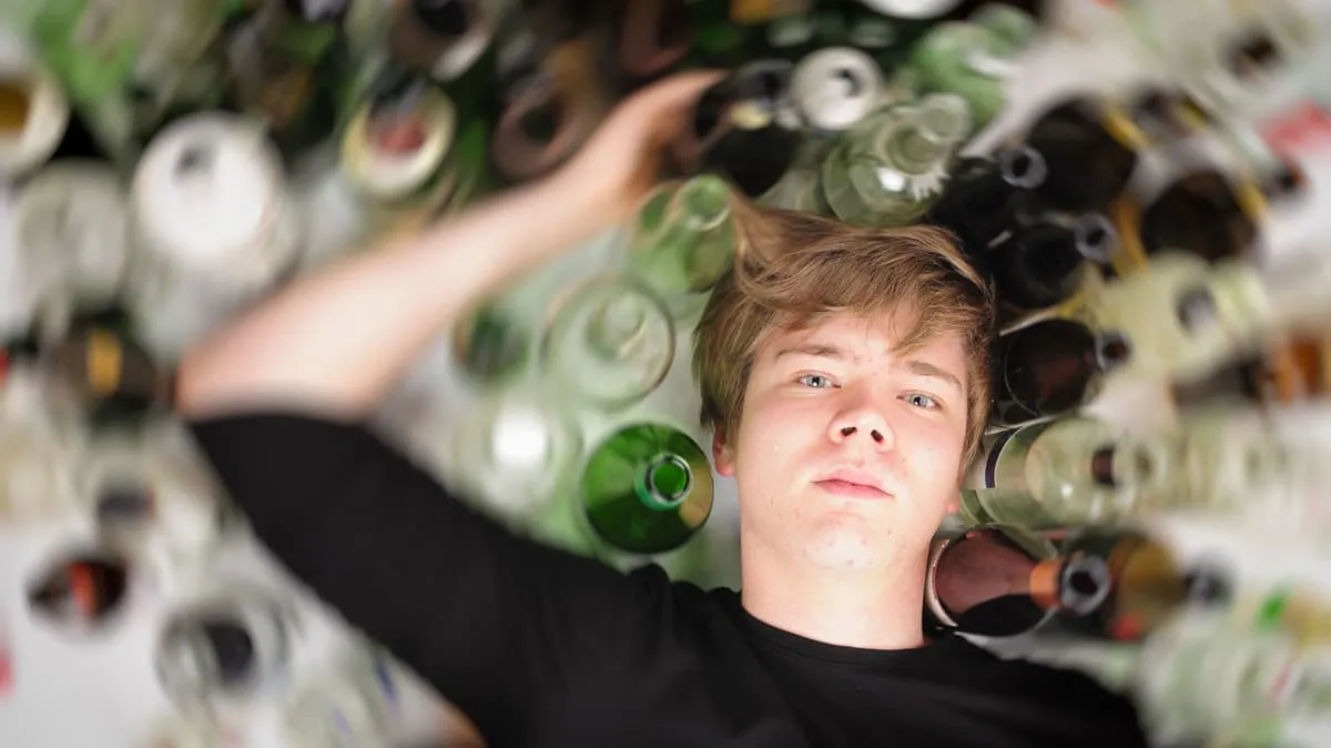 Joven rodeado de botellas vacías que representa el consumo de alcohol entre adolescentes.