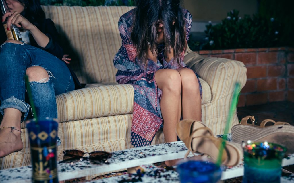Consecuencias del consumo excesivo de alcohol en jóvenes. Joven sentada en un sofá con la cabeza entre las manos, representando los efectos del consumo excesivo de alcohol.