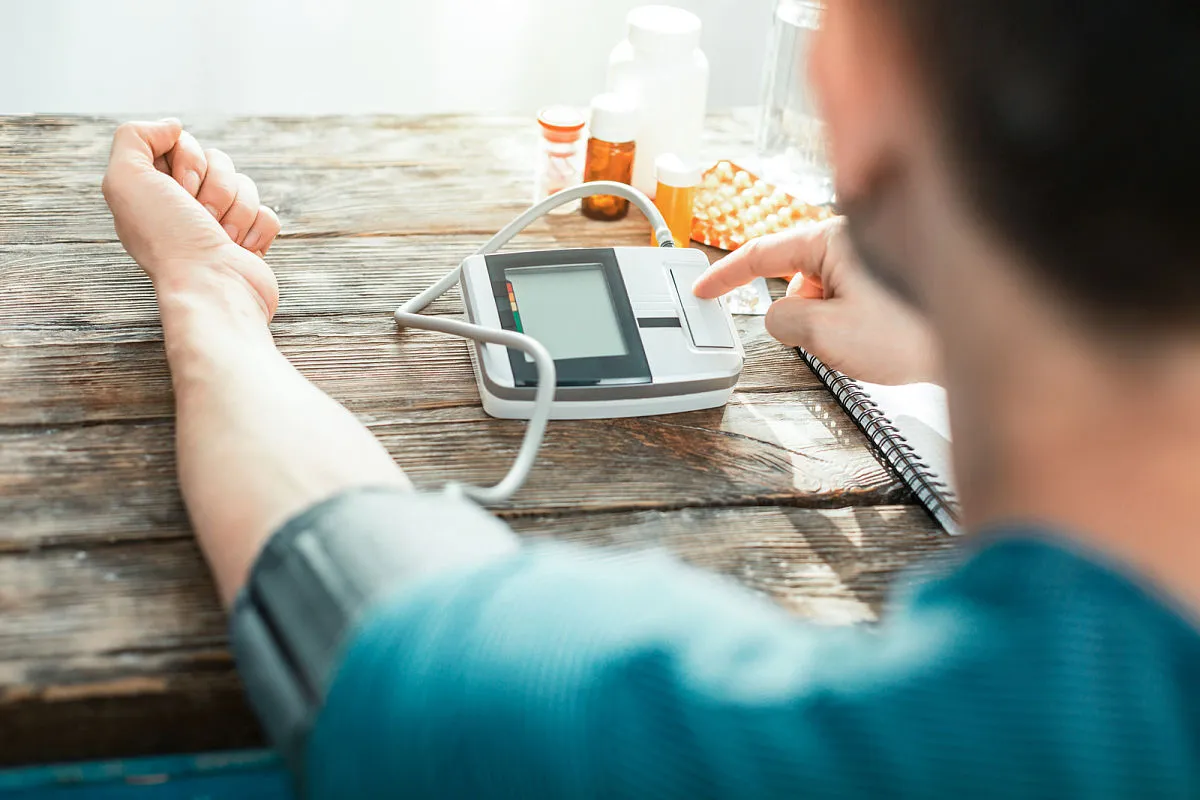 Hombre utilizando un baumanómetro digital para medir su presión arterial y controlar los efectos del exceso de sodio en la dieta