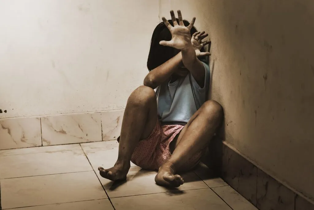 Niña asustada en una esquina protegiéndose con las manos, una imagen sobre las secuelas del trauma por abuso infantil.