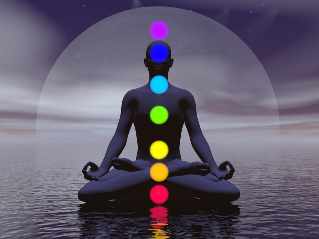 Alineación de chakras y equilibrio energético. Persona meditando con los siete chakras iluminados frente al agua, símbolo de equilibrio energético y bienestar.