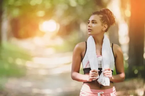 Mujer descansando con una toalla después de practicar deportes outdoors, un ejemplo de entrenamiento divertido y ecofriendly al aire libre.