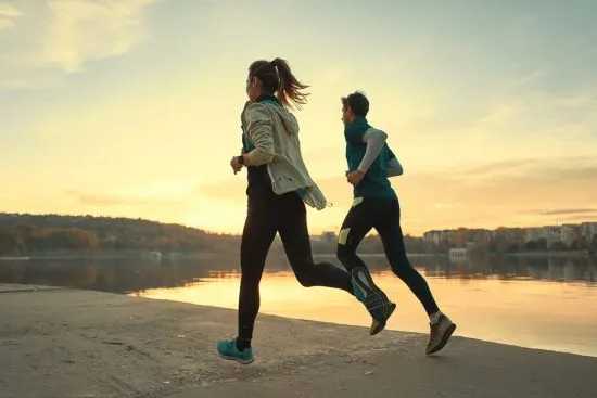 Pareja corriendo al aire libre junto a un lago como actividad física regular para combatir la hipertensión y reducir el estrés