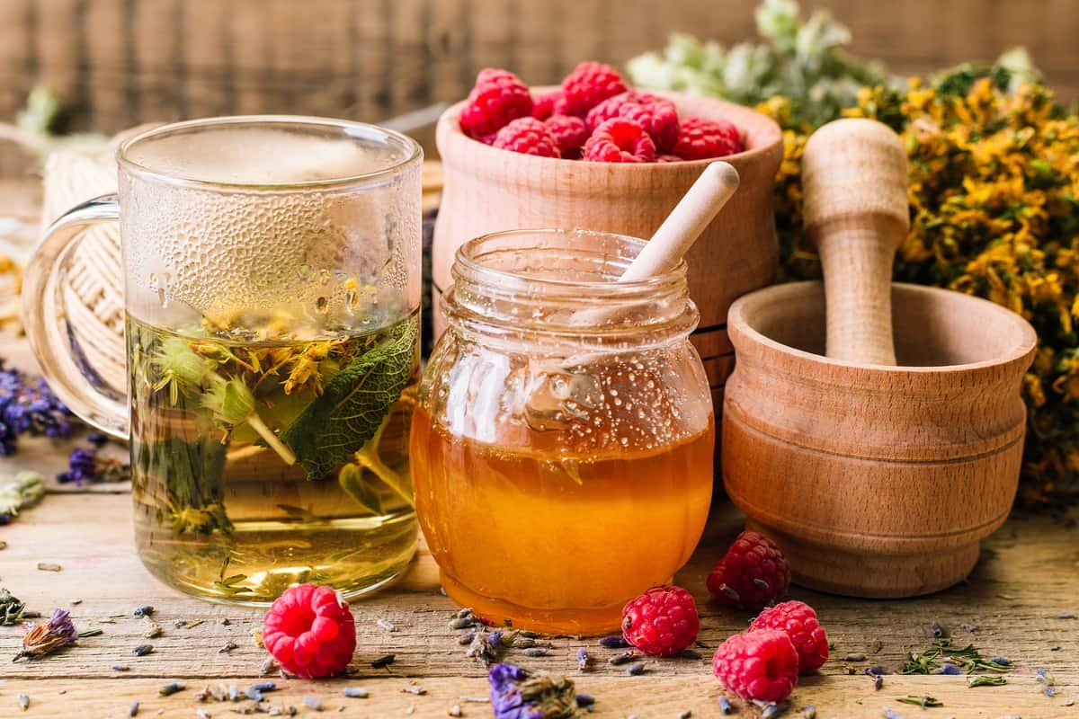 Infusión de hierbas naturales con miel, frambuesas y flores secas, sobre una mesa de madera rústica.