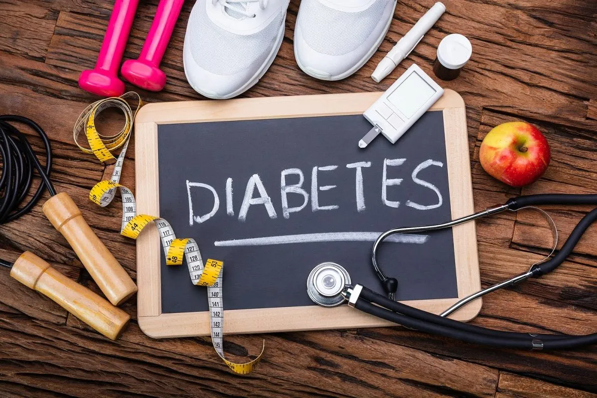 Pizarra con la palabra “diabetes” rodeada de elementos de salud y ejercicio como un estetoscopio, una cuerda para saltar, pesas, un glucómetro y una manzana.