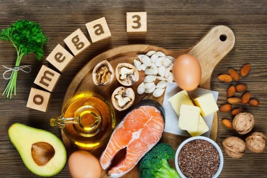 Fuentes naturales de omega-3: pescado, semillas y frutos secos. Alimentos naturales ricos en omega-3: salmón, aguacate, nueces, aceite vegetal y semillas sobre tabla de madera.