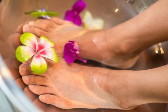 Pies sumergidos en agua con flores tropicales durante un tratamiento de spa.