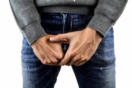 Hombre con las manos sobre la zona pélvica, expresando incomodidad o preocupación.