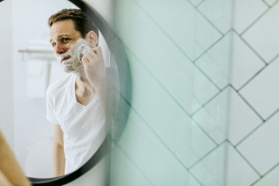 El Poder de tu Rutina de Mañana: Prepara tu Día con Intención. Hombre afeitándose frente al espejo, como parte de una rutina de mañana para empezar el día con energía.