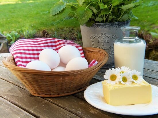 Ingredientes frescos para un desayuno de campo: una cesta de huevos, leche y mantequilla sobre una mesa de madera.