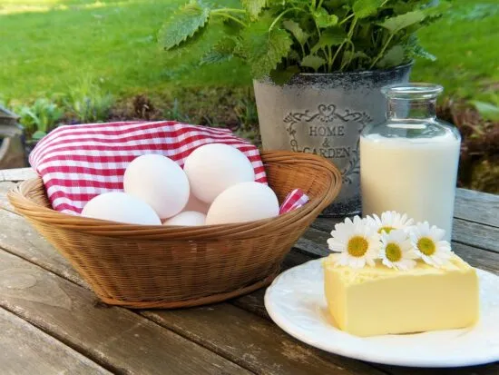 Ingredientes frescos para un desayuno de campo: una cesta de huevos, leche y mantequilla sobre una mesa de madera.