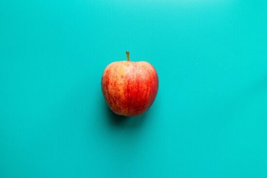 Una manzana roja y fresca sobre un fondo turquesa, simbolizando los beneficios de esta fruta para la salud del colon.